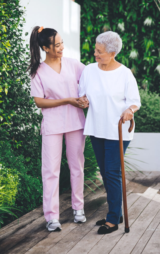 nurse smiling and helping older lady that has a cane