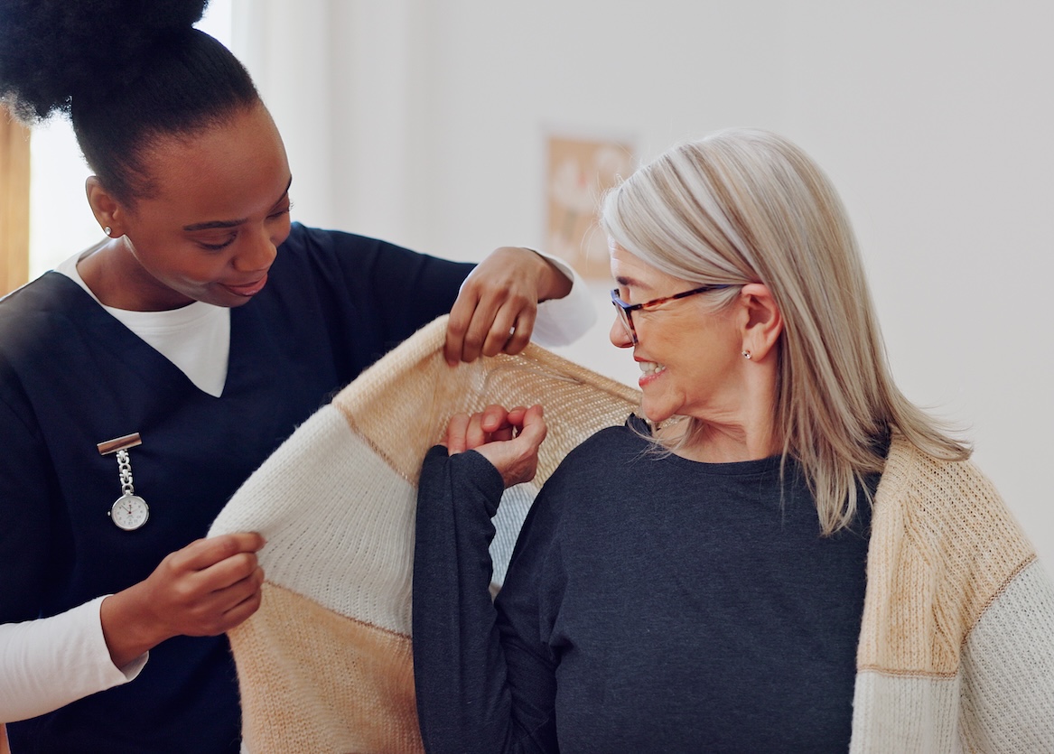 Senior woman, nurse and help with clothes, smile and care in retirement, nursing home and support.